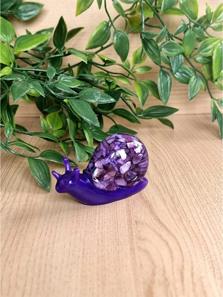 A detailed purple resin snail sculpture with a shell crafted from small, glittering amethyst-like shards, resting on a light wood surface.