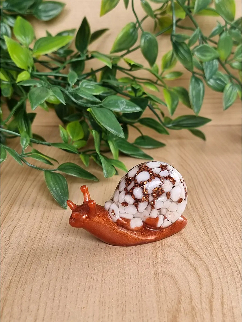 A charming handcrafted resin snail sculpture with a glossy copper body and a unique shell composed of white pebbles and bronze glitter.