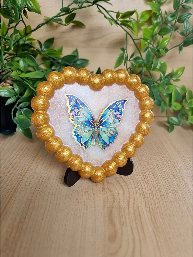 A golden beaded heart resin art piece with a blue holgraphic butterfly.