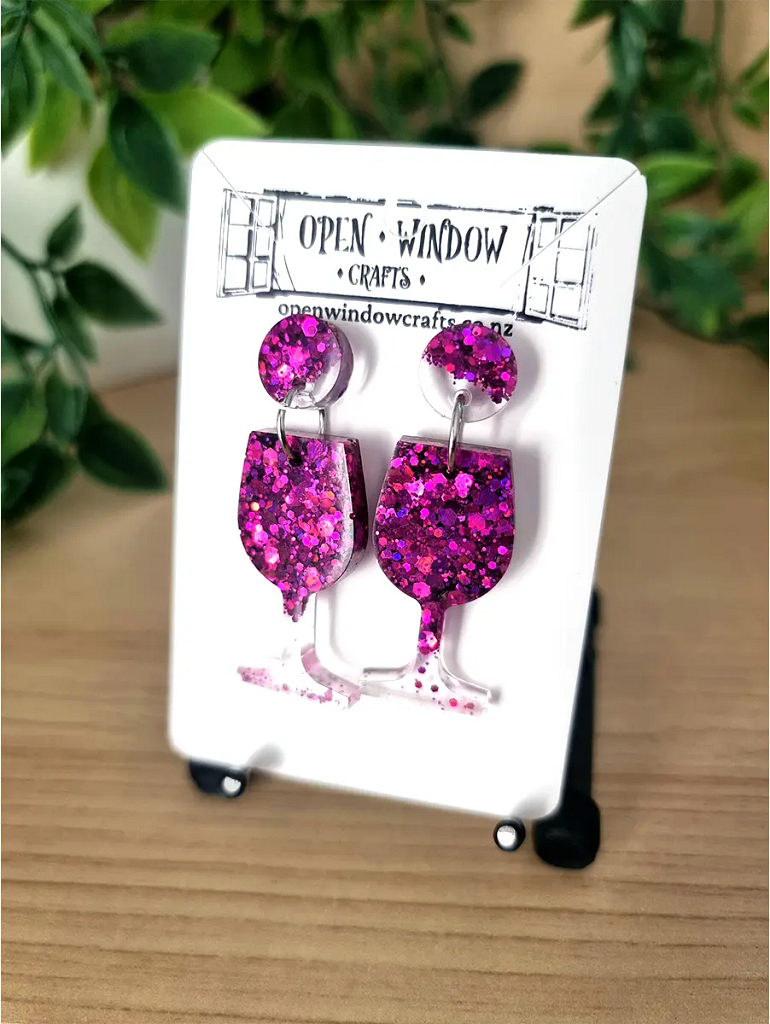 Magenta glitter wine glass earrings dangle from silver hooks, showcasing a festive, sparkling design.