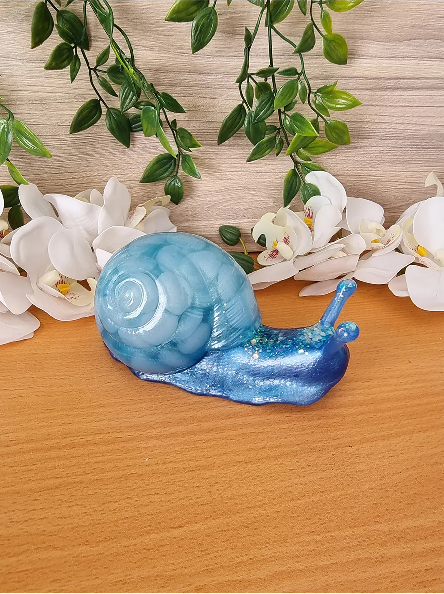 A handcrafted resin sculpture of a snail with a swirling blue shell and a shimmering blue body, adorned with glitter accents.