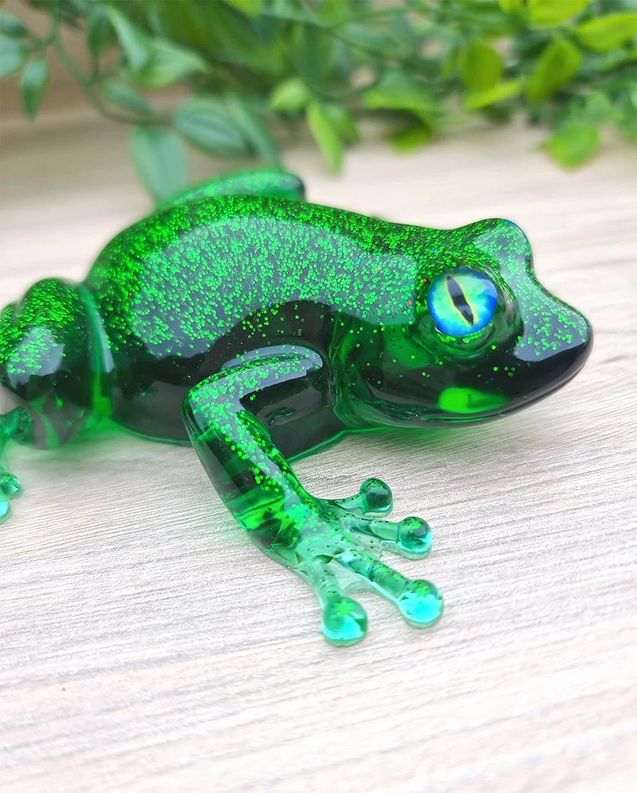 A handcrafted emerald green resin frog with sparkling glitter on its back and captivating blue-green eyes.