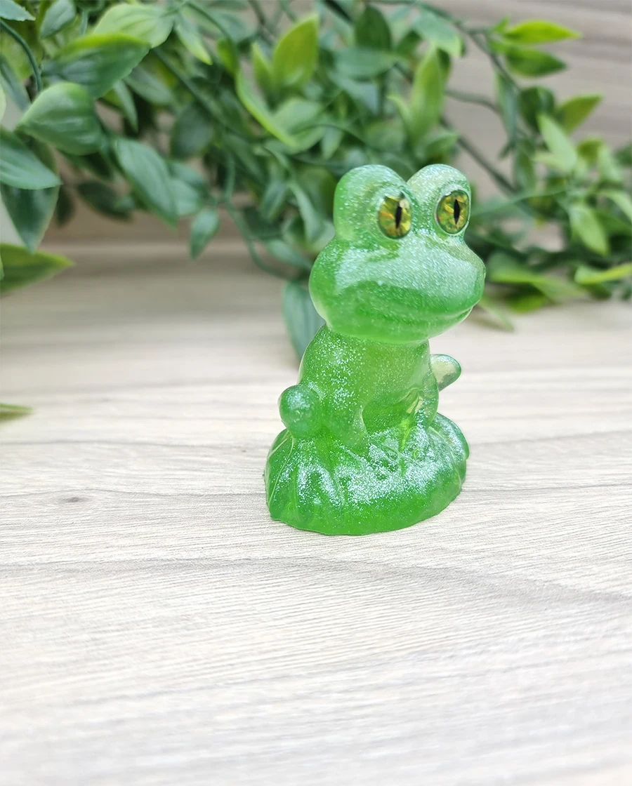 A charming, translucent, glittery green resin frog figurine with captivating yellow eyes, crafted as a delightful miniature.