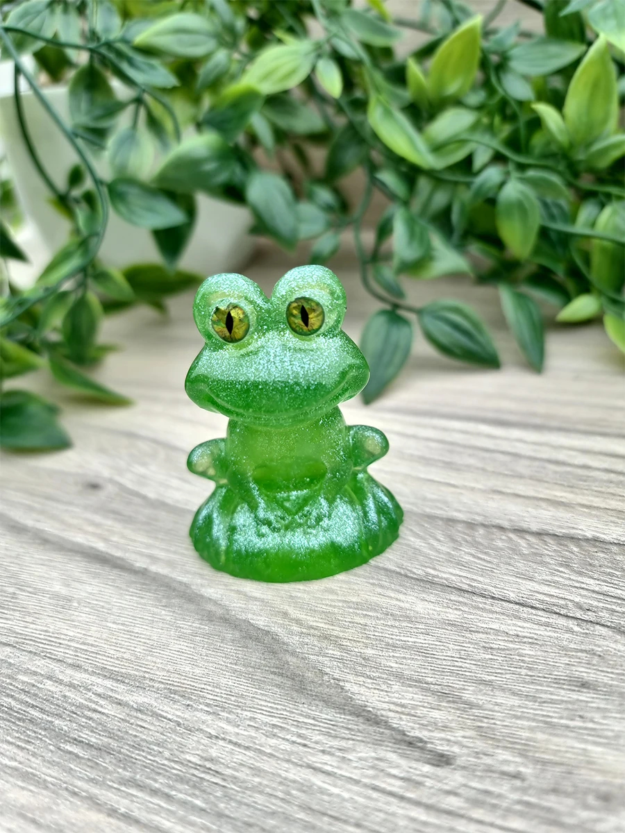 A translucent emerald green resin frog figurine with striking yellow eyes glistens with a subtle shimmer.