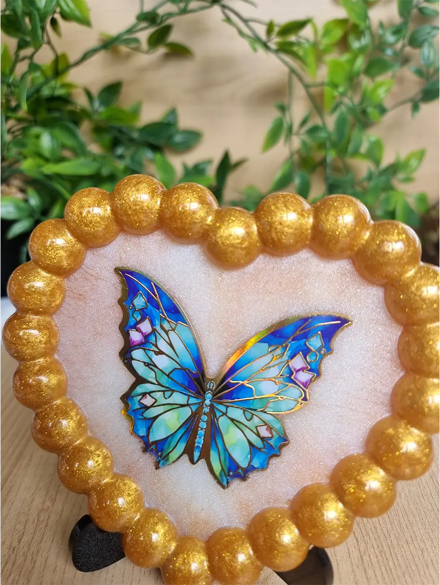 Heart-shaped resin coaster with gold beaded edge and blue butterfly detail.