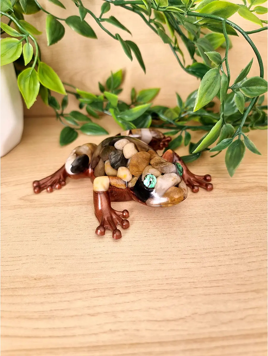 A unique resin art piece depicting a frog with its body artfully inlaid with real natural stones and featuring striking green jade eyes.