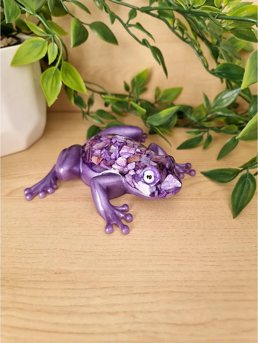 A shimmering purple frog sculpture with crushed shell accents and detailed eyes, resting on a wooden surface.