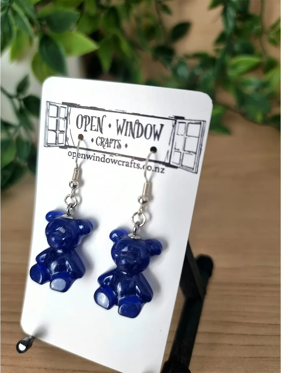 A pair of deep sapphire blue gummy bear shaped resin earrings dangle from silver hooks.
