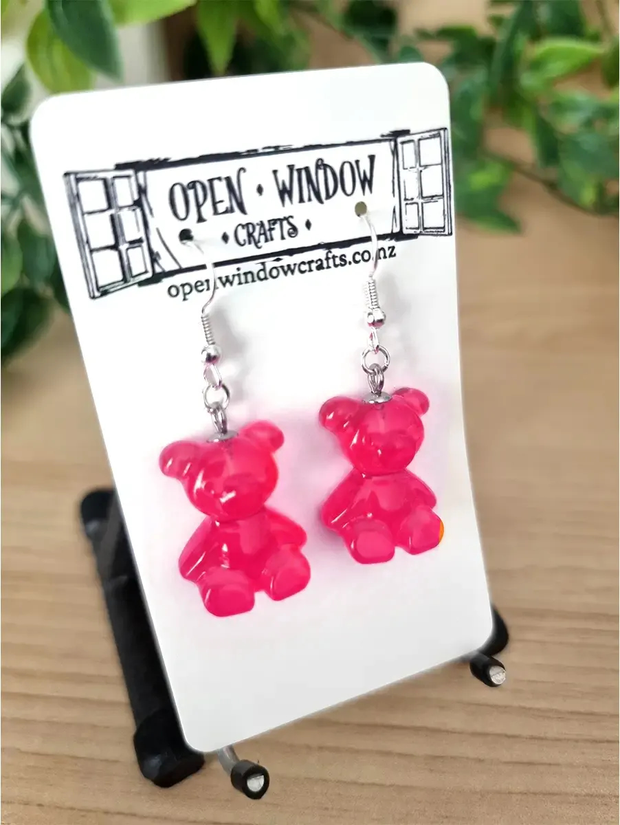 Two vibrant hot pink gummy bear dangle earrings with silver hooks displayed on a white card.