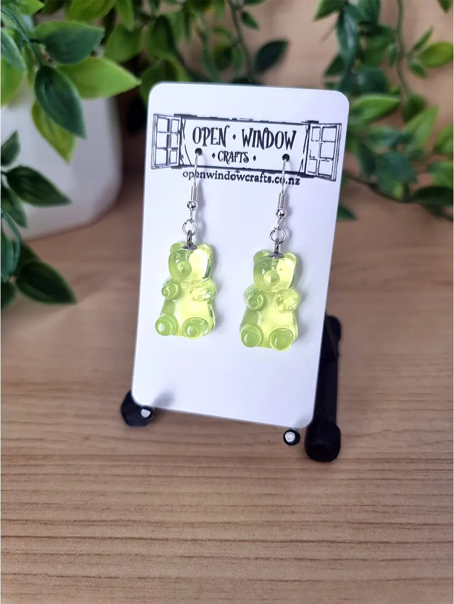 Neon yellow gummy bear resin earrings dangle from silver hooks, presented on a branded card.