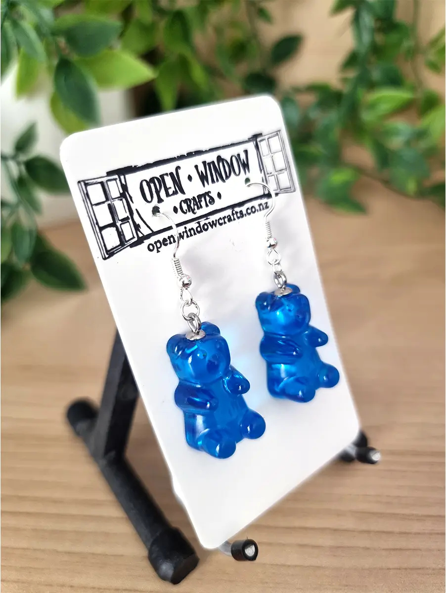Vibrant blue gummy bear shaped resin earrings dangle from silver hooks, presented on a white card.