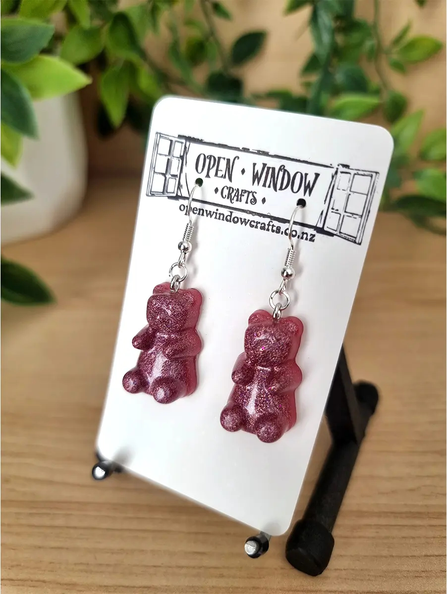 Raspberry gummy bear resin earrings shimmer with glitter and hang from silver hooks.