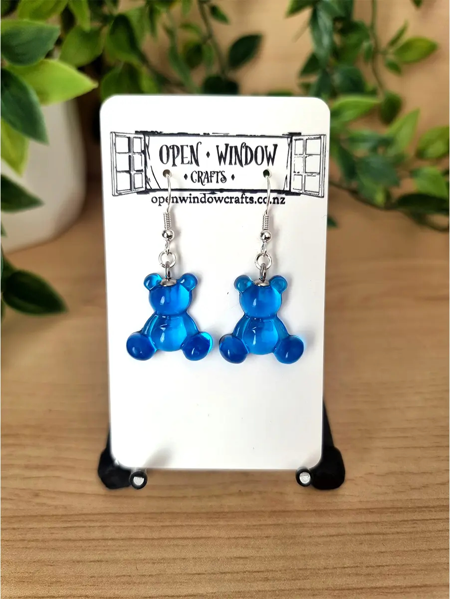 Translucent blue gummy bear earrings dangle from silver hooks. Artisan crafted for unique gift ideas.