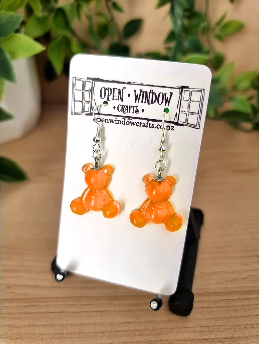 Translucent Orange gummy bear resin earrings hang from silver hooks on a white display card.