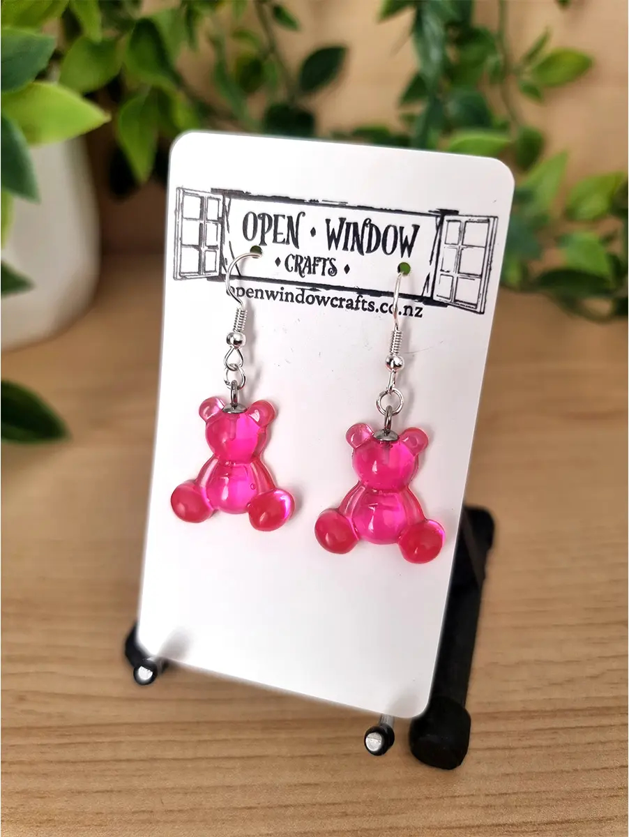 Translucent pink gummy bear earrings hang from silver hooks, presented on a white branded card.