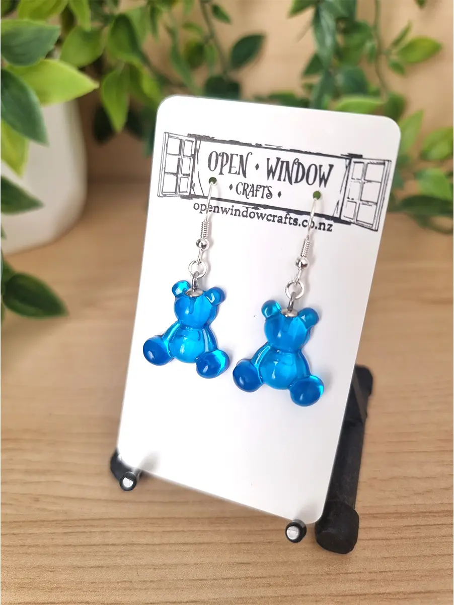 Translucent blue gummy bear resin earrings dangle from silver hooks, presented on a white Open Window Crafts card.