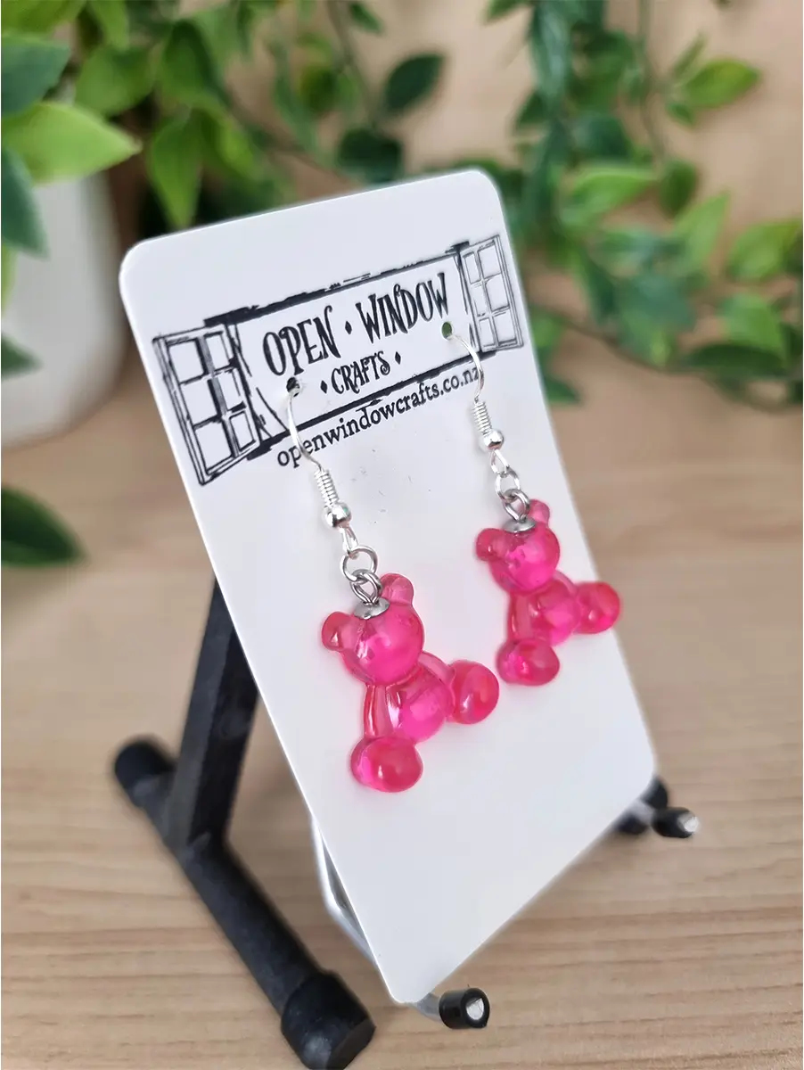 Hot translucent pink gummy bear earrings place s on a branded card looking very sparkly.