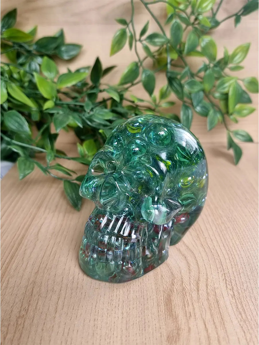 Marble resin skull sculpture with internal red flecks sits on a wooden surface with green foliage in the background.