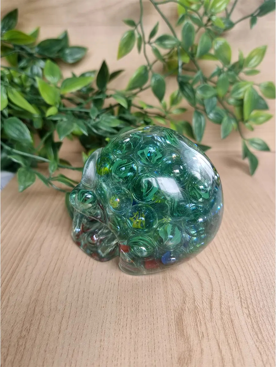 Resin skull sculpture filled with marbles rests on a wooden surface.