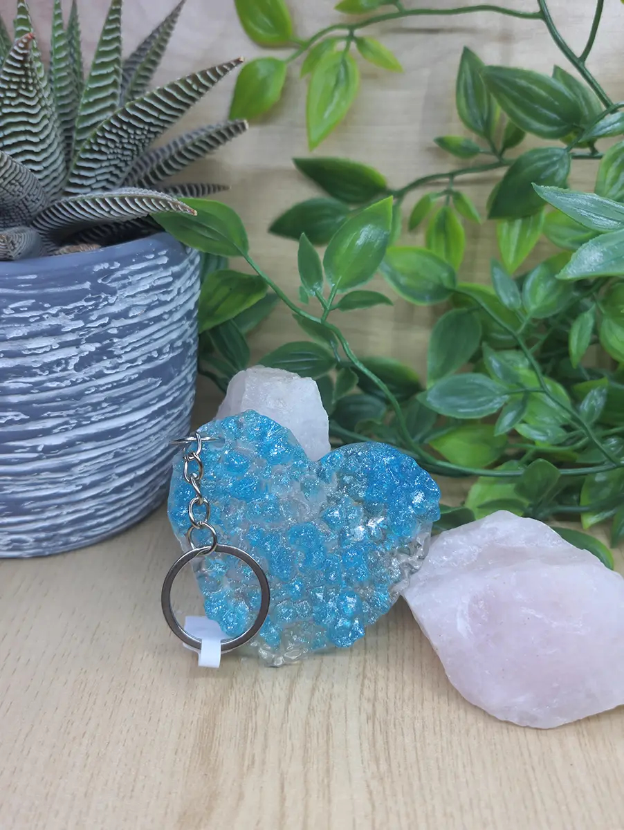 Sparkling aqua blue resin heart keychain with a clear, crystalline texture and silver hardware rests on wood.