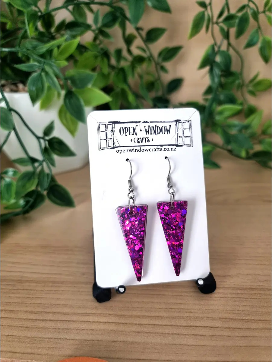 Triangular pink glitter resin dangle earrings shimmer with iridescent flakes on surgical steel hooks.