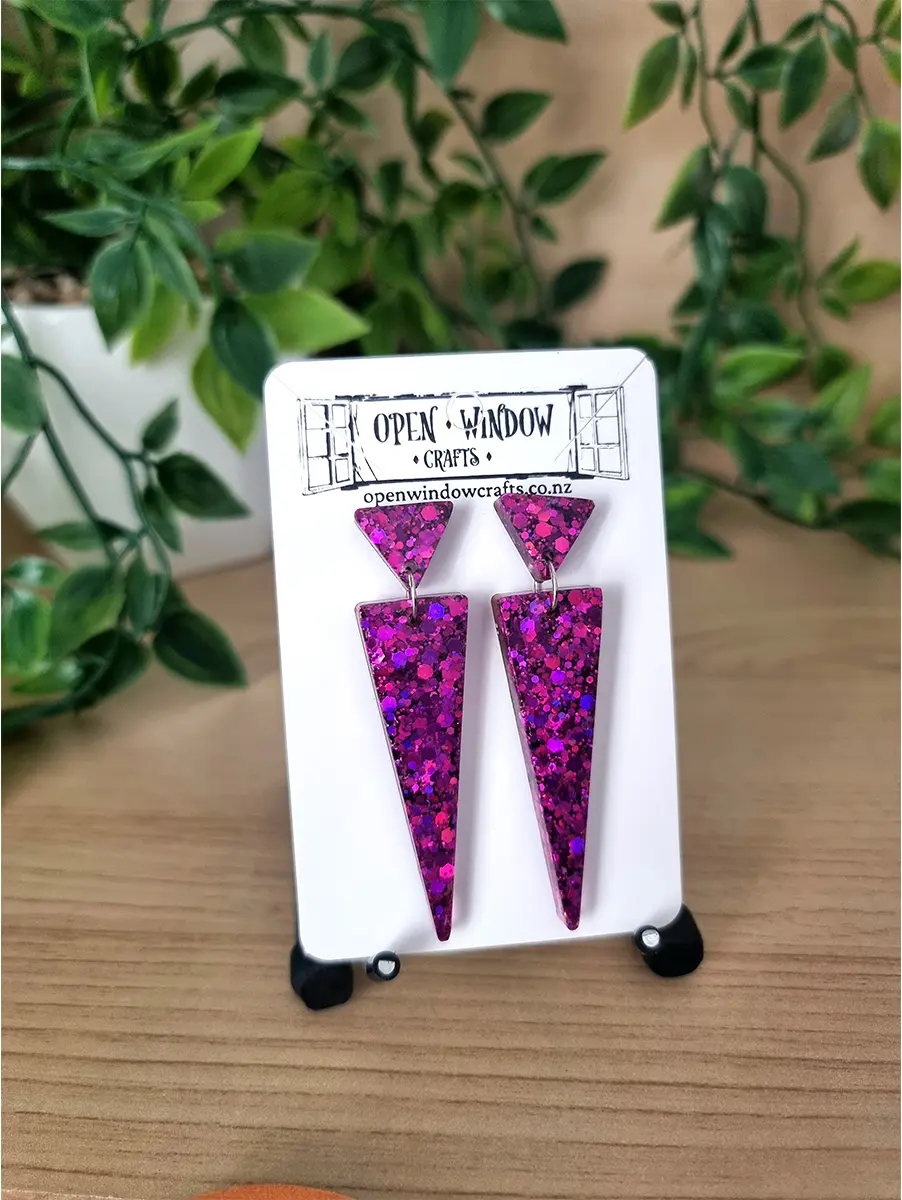 Geometric fuchsia glitter earrings dangle from silver hooks on a white card.