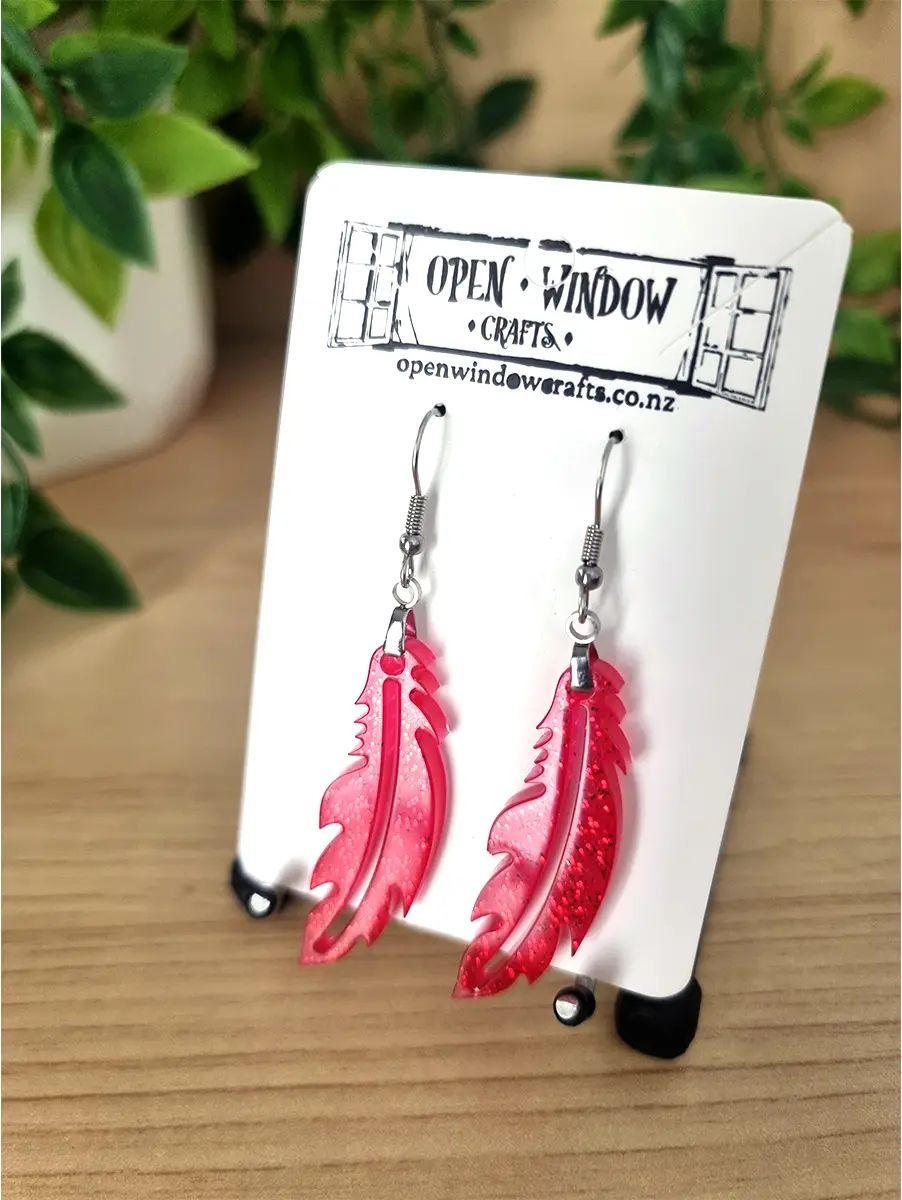 Sparkling red feather resin earrings dangle from silver hooks, handcrafted by Open Window Crafts in New Zealand.