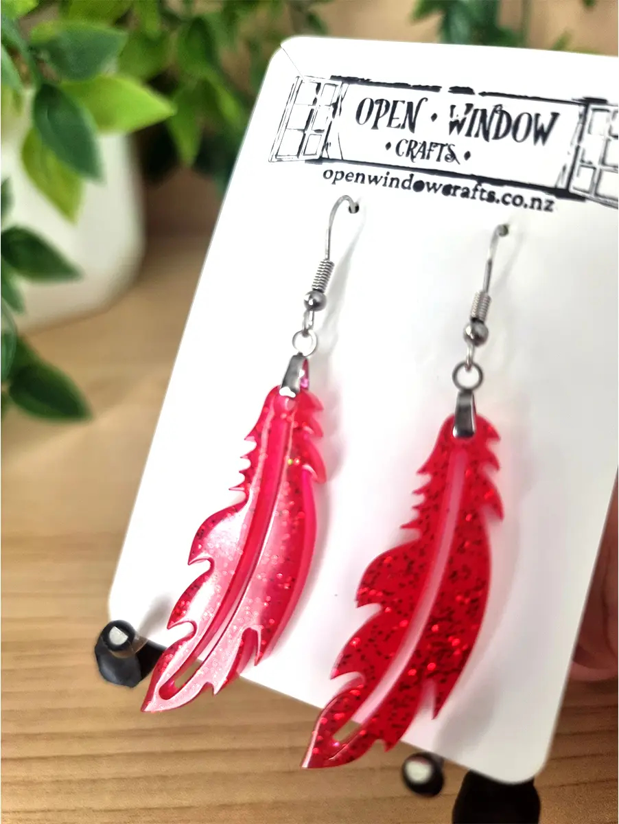 Sparkling red resin feather earrings dangle from silver hooks.