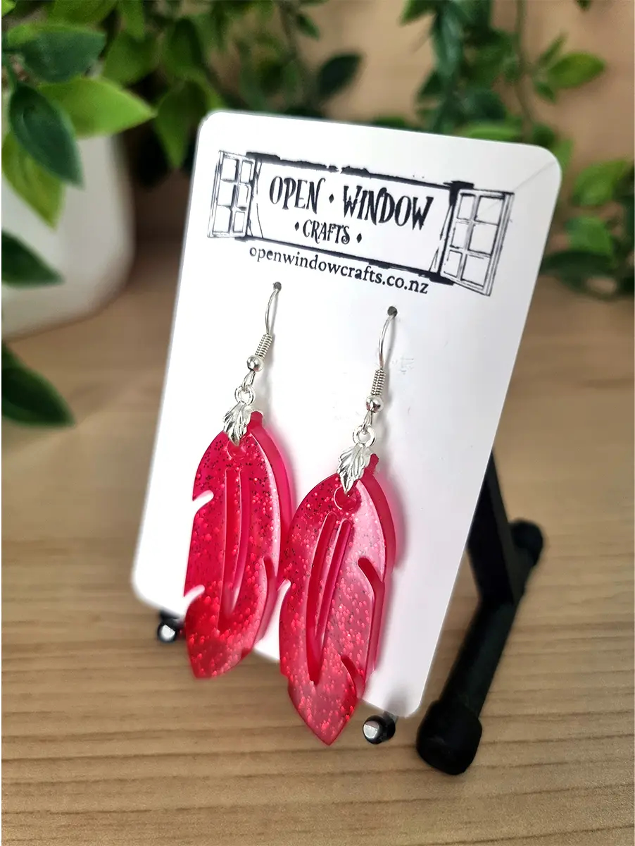 Red glitter resin feather drop earrings dangle from silver hooks.