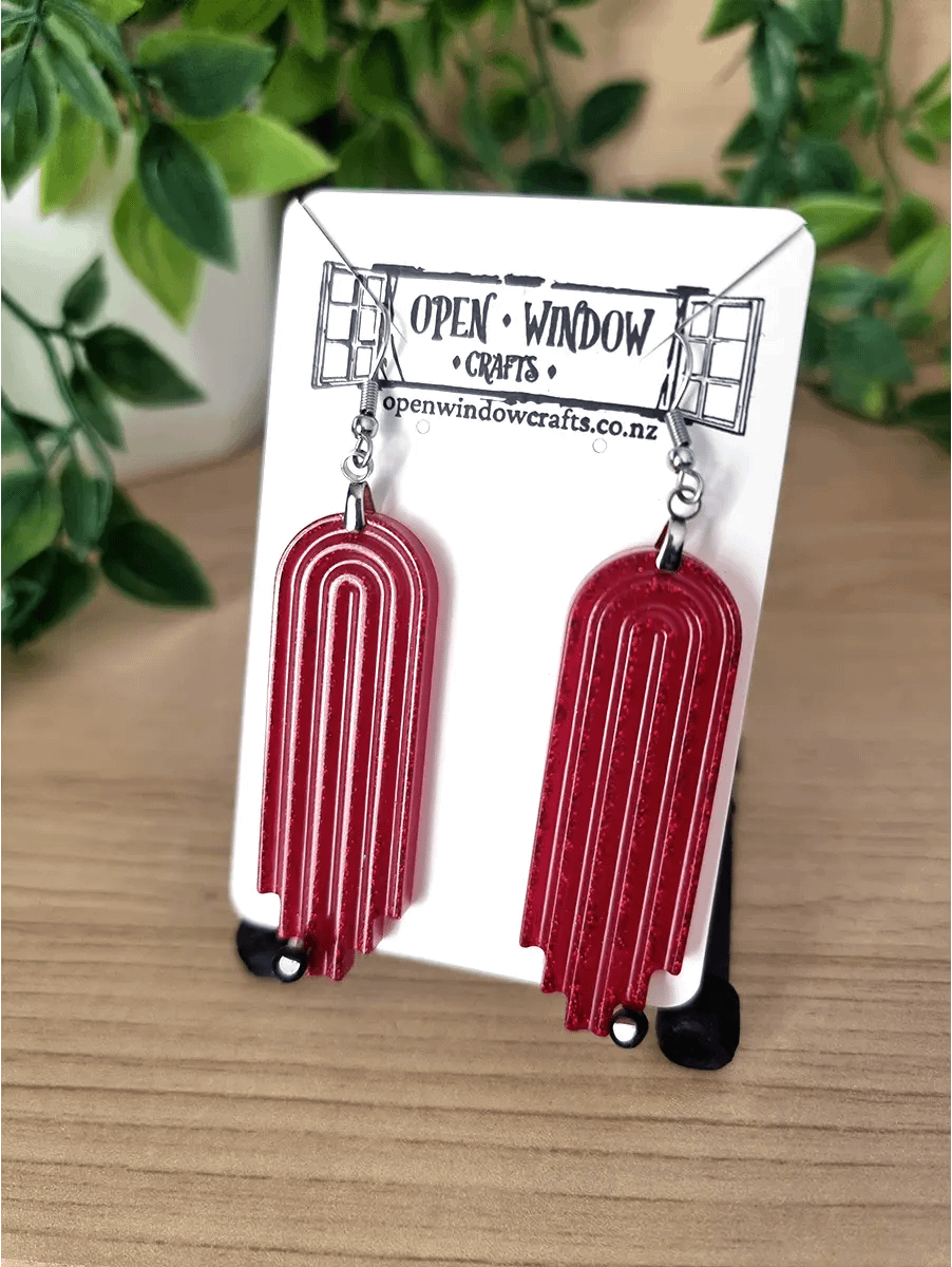 Red geometric arch earrings with a subtle glitter inlay hang from silver hooks.